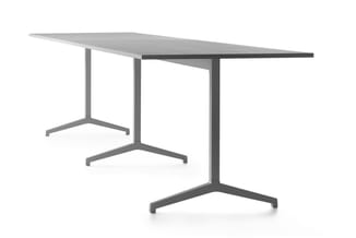 Grijze vergadertafel met schuine tafelblad en drie poten met driehoekige voetplaatjes, frontaanzicht.