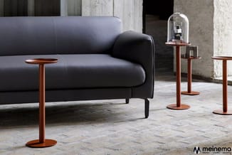 Zwarte leren sofa met houten armleuningen en bijzettafels met houten zuiltafels in een betonnen industriële ruimte.