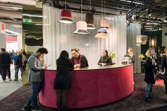 Ronde baliebalie in bordeauxrood met drie medewerkers, hangende design-lampen in rood, roze en geel, in moderne kantoorruimte