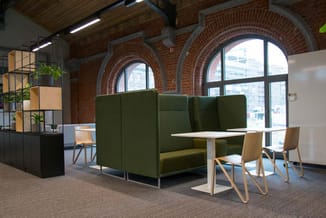 Groen akoestische zithoek met hoge zijwanden in kantoor met bakstenen wanden, grote ramen en houten stoelen aan witte tafel.