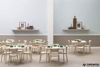 Moderne kantine met lichte houten eettafels en beige stoelen, groene borden, twee wandplanken met keukenaccesoria boven grijz