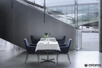Moderne vergadertafel met wit tafelblad en zwart kruisonderstel, omgeven door vier donkerblauwe stoelen in een ruimte met gri