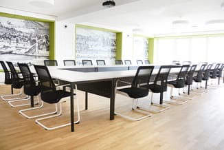 Moderne vergaderruimte met lange witte vergadertafel, zwarte mesh-stoelen met witte frames, houten vloer, witte plafonds en g