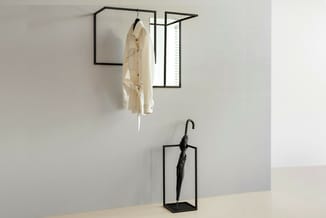 Zwarte stalen wandgarderobe met spiegeldetail en hangende beige jas, daaronder staande parapluhouder met zwarte paraplu op ta