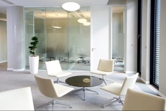 Modern kantoorruimte met vier witte loungestoelen rond zwarte ronde tafel, glazen vergaderruimte op achtergrond, hangende ver