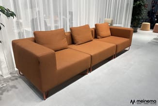 Modulaire oranje bank met drie zitdelen, houten poten, losse kussens, in minimalistische witte ruimte met gordijnen.