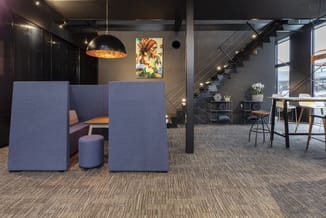 Blauwe akoestische wanden in open kantoorruimte met zwarte hanglampen, trap en werkplekken op achtergrond.