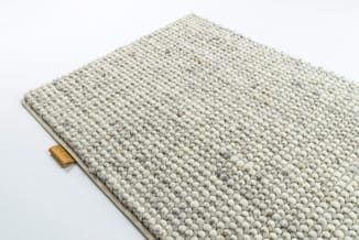 Grijsbeige structuurstof met bolletjestextuur en houten label aan zijkant, waarschijnlijk stoffaal of materiaalmonster.