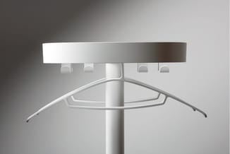 Witte garderobe staander met rond centrale paal, brede bovenplank en gebogen hangers onderaan tegen neutrale achtergrond.