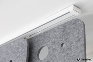 Witte akoestische wandpanelen in grijs vilt met ronde gaten, opgehangen aan wit profiel tegen witte wand.