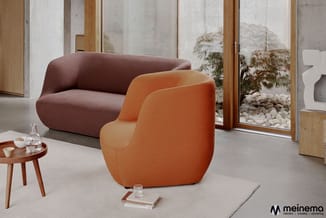 Twee ronde fauteuils in oranje en bordeaux in minimalistisch interieur met houten tafel, glazen deuren naar tuin en witte scu