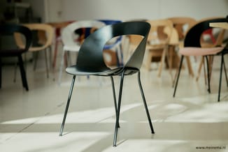 Zwarte design stoel met gebogen kunststof zitting en metalen poten in showroom met houten en witte stoelen op achtergrond.