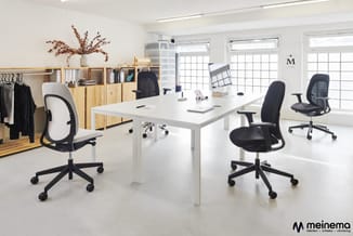 Modern kantoor met witte vergadertafel, drie zwart-grijze bureaustoelen, houten kasten met ophangsysteem, droogkast en grote