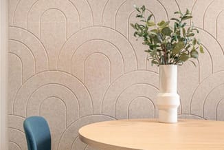 Ronde houten tafel met blauwe stoel en witte vaas met groen, voor behang met geometrisch patroon.