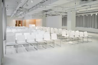 Moderne vergaderruimte met witte stapelstoelen op chromen frames, rijen gericht naar podia met oranje/gouden wanden, helwit p