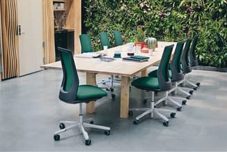 Vergaderruimte met lichte houten tafel, groene ergonomische bureaukstoelen met wielen, levensmuur op achtergrond, houten kast