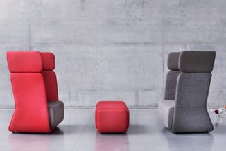 Drie modulaire zitmeubels tegen betonnen wand: rode fauteuil met hoofdsteun, rode poef, grijze fauteuil met hoofdsteun.