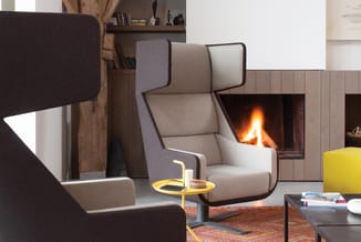 Moderne loungehoek met grijsbeige fauteuil met hoofdsteun, zwarte bijzettafel, gele staande lamp en open haard in houten wand