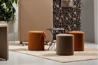 Vier ronde poefzitels in bruin en grijs wol op beige tapijt in moderne kantoorruimte met tekstbehang en plant.