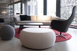 Moderne lounge met beige sofa, witte poefzit, zwarte fauteuil, ronde tafel, rode tapijt en hangende kristallen lamp.