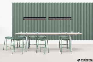 Lange houten vergadertafel met witte onderstel en zes groene barkrukken tegen groene geribde achterwand met twee zwarte airco