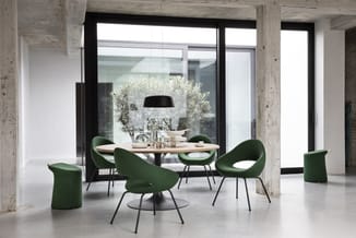 Moderne vergaderruimte met ronde tafel, groene stoelen met zwarte poten, hangende zwarte lamp, betonnen kolommen en grote raa