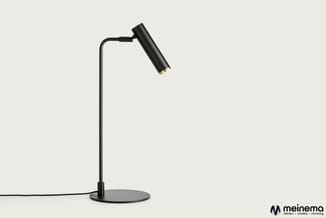 Zwarte bureaulamp met ronde voet, lange stam en verstelbare lampenkop op grijze achtergrond.