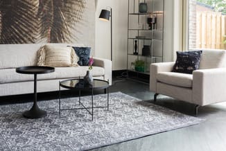 Modern woonkamer met beige banken, zwarte bijzettafels, grijze tapijt, metalen staande lamp en open wandkast met planken.