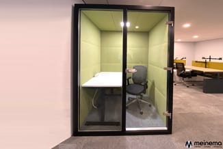 Glazen belcel met gele wanden, zwart frame, wit werkblad, grijze bureaustoel en LED-verlichting in modern kantoor.