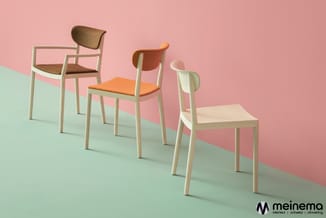 Drie houten stoelen met lichte framestructuur op mint groen oppervlak tegen roze muur. Stoelen hebben bruine, oranje en natur