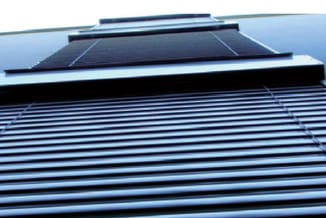 Zwart golfkartonnen dak met zonnepanelen en blauwe metallieke dakbedekking tegen hemelblauwe achtergrond.