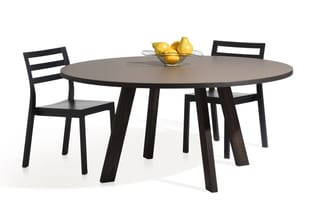 Ronde zwarte eettafel met grijsbruinblad en twee bijpassende zwarte stoelen met horizontale rugsteun. Glazen schaal met gele