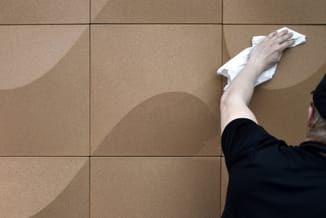 Person reinigt beige wandpaneel met wit doek, toont onderhoud van akoestische wandbekleding.