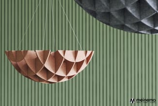 Terracotta-kleurige hanglamp met origami-achtig papieren design tegen groene golfplaten wand.