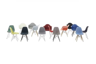 Elf moderne stoelen in verschillende kleuren en uitvoeringen, gerangschikt op een rij. Gekleurde zittingen in groen, wit, zwa