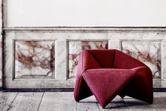 Rode stoffen fauteuil met draaibare basis in minimalistische kamer met marmeren wanden en houten vloer.