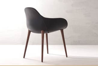 Moderne stoel met zwart kunststof zitting, gebogen rugleuning en donkerbruinen houten poten in minimalistische ruimte.