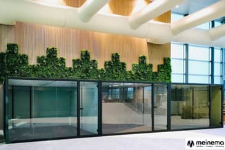 Kantoor met glazen wanden, groene wandbeplanting, houten latten wandbekleding, wit plafond met ronde buizen en skylight.