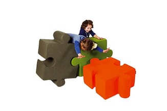 Twee kinderen spelen op gekleurde puzzelstukken meubels in grijs, groen en oranje tegen witte achtergrond.