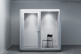Glazen belcel met witte aluminium frame, twee compartimenten, linker deur gesloten, in rechter ruimte zwarte stoel, grijze mu