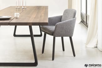 Houten eettafel met zwart metalen onderstel en grijze gestoffeerde stoel met armleggers in minimalistisch interieur.