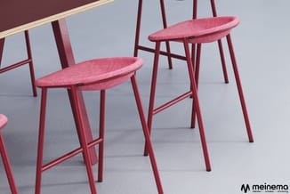Rode barstoel met roze geweven zitting en metalen frame, in rij geplaatst tegen grijze wand met houten rail.