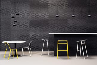 Moderne kantoorruimte met ronde tafel, gele en grijze stoelen, bartafel met gele barkruk, hangende zwarte lampen en perforeer