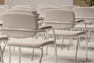 Witte gestoffeerde stoelen met metalen frame en schrijftablet, opgesteld in rijen in een vergaderruimte.