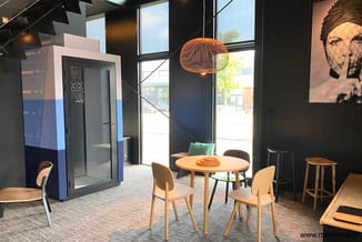 Moderne kantoorruimte met ronde houten tafel, houten stoelen, hanglamp met oranje spiraalkabel, blauwe akoestieke belcel, gro