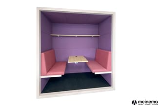 Belcel met paarse wanden, roze zitbanken aan weerszijden, houten tafel in het midden, metalen stang bovenaan, donkere vloer.