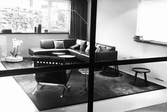 Modern kantoor in zwart-wit met zwarte leren hoekbank, zwarte eettafel, designstoelen en zwarte tapijten. Grote ramen met gor