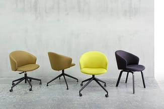 Vier bureaustoelen in verschillende kleuren (beige, olijfgroen, geel, zwart) met wieltjes en draaibare zitting op betonachtig