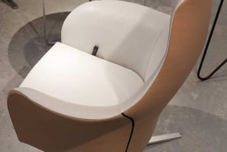 Moderne stoel met cognackleurig leer aan de zijkanten en wit/crème zitting, op grijs betonachtig vloermateriaal.