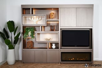 Grijs-bruine wandkast met geopende vakken, witte displaykasten, TV-scherm en elektrische haard. Houten accessoires en groene